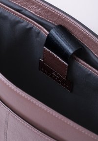 Brown leather tote bag interior with dark fabric lining, featuring a rectangular label patch and smooth texture along the edges.