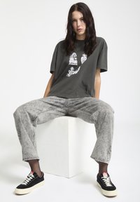Camiseta oversized gris oscuro con estampado gráfico blanco, combinada con jeans gris claro y zapatillas negras con acentos blancos.