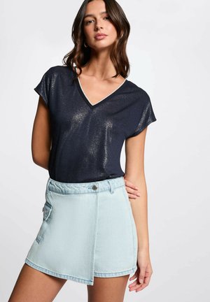 Top a V scollo navy con un leggero luccichio abbinato a una gonna a portafoglio in denim azzurro chiaro con tasca frontale e dettaglio dei bottoni.