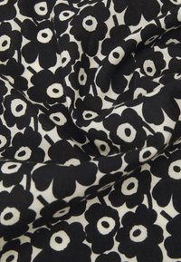 Tissu noir et blanc présentant un motif floral avec de grandes fleurs noires et des centres circulaires sur un fond crème, mettant en valeur une texture douce.