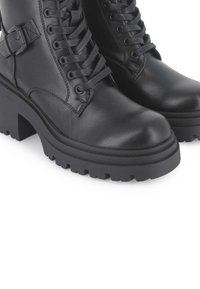 Botas de tobillo de cuero negro con suelas gruesas y con dibujo, puntera redonda y cordones en la parte delantera. Presentan un detalle en forma de hebilla lateral para un toque adicional.