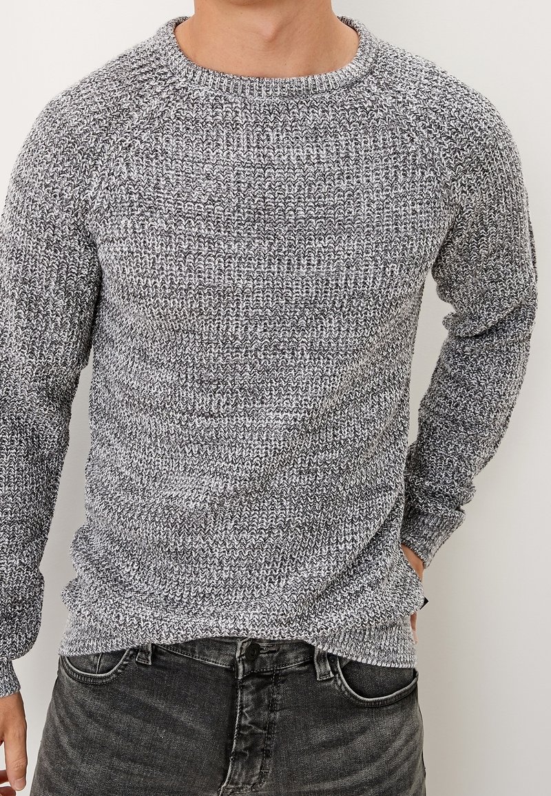 Grau gemusterter Strickpullover mit Rundhalsausschnitt und langen Raglanärmeln, der aus einem strukturierten, weichen Stoff besteht und zu dunklen Jeans passt.