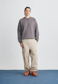 Gray cotton sweatshirt with a crew neck, beige cargo pants, and orange shoes with laces. The outfit features a relaxed fit and utility pockets.