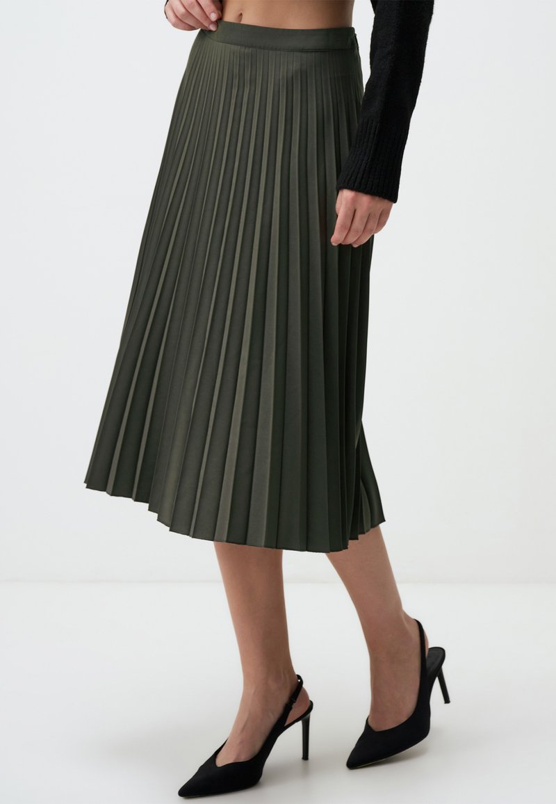 Faltender Midi-Rock in Olivgrün, aus strukturiertem Material, mit einem taillierten Bund und einem fließenden Design, kombiniert mit schwarzen High Heels.