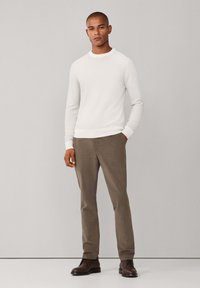 Maglione grigio chiaro con colletto a giro, abbinato a pantaloni marrone chiaro e scarpe marrone scuro. Il tessuto sembra liscio e aderente.