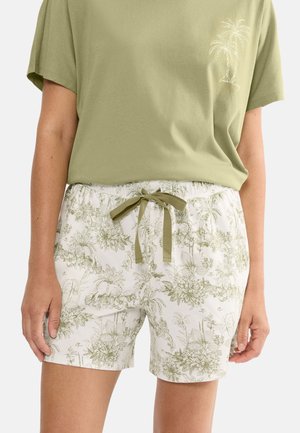 Oliwkowa zielona koszula z nadrukiem palm w zestawieniu z białymi szortami ozdobionymi zielonymi kwiatowymi i roślinnymi wzorami oraz oliwkowym sznurkiem.