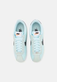 Sneaker azzurri chiari con uno swoosh nero, dettagli grigi e lacci texture. Parte superiore in pelle liscia con collare imbottito per il comfort.