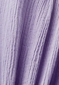 Tissu violet clair avec une texture froissée verticale, des plis doux et des ombres subtiles mettant en valeur la surface irrégulière.
