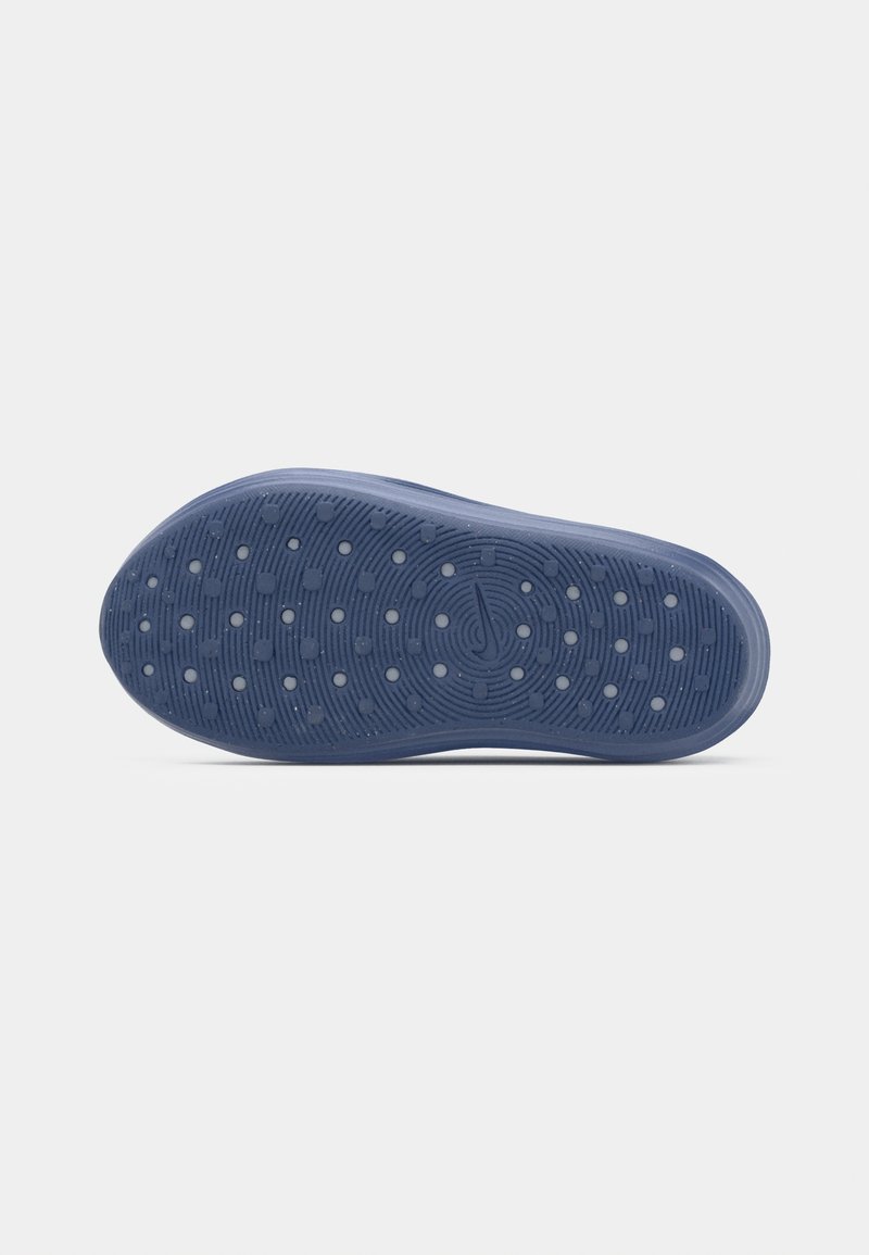 Suela de una zapatilla azul con patrones circulares y de puntos para tracción, mostrada sobre un fondo blanco liso.