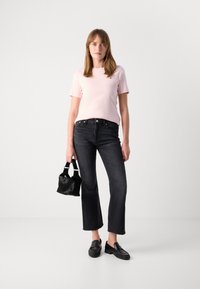 Lys rosa t-skjorte med korte ermer, sorte høy midje jeans, sorte loafers og en liten svart håndveske med teksturert overflate.