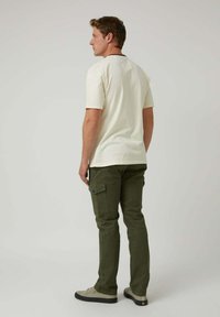 Camiseta de manga corta color crema con cuello redondo, combinada con pantalones cargo en verde oliva que cuentan con bolsillos laterales y detalles en negro.