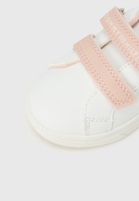 Λευκό αθλητικό παπούτσι με ροζ λουριά βέλκρο, λείο συνθετικό υλικό, στρογγυλεμένη μύτη και λογότυπο στην κορδέλα.