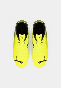 Φωτεινά κίτρινα ποδοσφαιρικά παπούτσια με μαύρες λεπτομέρειες, που διαθέτουν κομψό σχέδιο, επίπεδα κορδόνια και εξέχον λογότυπο Puma στις πλευρές.