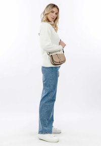 Pullover crema con texture; jeans azzurri a vita alta; sneaker bianche; piccola borsa beige a forma curvata con dettagli in metallo argentato.