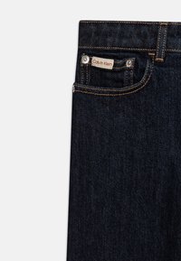 Jeans de mezclilla azul marino con corte recto, cuentan con costuras naranjas, un pequeño bolsillo frontal y una etiqueta de Calvin Klein en la cintura.