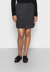 Jupe en laine gris foncé à coupe droite, avec deux poches avant et une texture lisse, accompagnée de chaussures en cuir noires avec un détail de boucle.