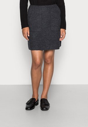 Jupe en laine gris foncé à coupe droite, avec deux poches avant et une texture lisse, accompagnée de chaussures en cuir noires avec un détail de boucle.