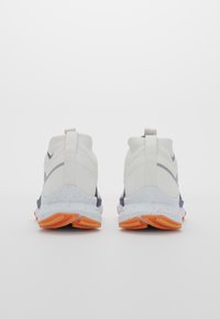 Baskets de course blanches avec un dessus lisse, accents gris et une semelle bleu tachetée avec des patins de traction orange. Tirant standard à l'arrière.
