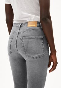 Grå denimjeans med slim fit, med en läderetikett märkt "ARMEDANGELS" och två bakfickor med sömdekorationer.
