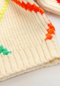 Tissu en tricot à côtes crème présentant des motifs géométriques colorés en vert, orange et jaune, avec une finition texturée et un toucher doux.