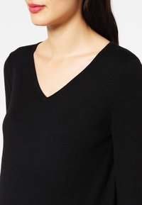 Pull en tissu noir avec un col en V et des manches longues, doté d'une texture douce et d'une coupe slim.