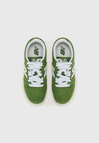 Zelene suede tenisice s bijelim vezicama, perforirani dizajn na prednjem dijelu i teksturirana bijela potplata. New Balance logo na jeziku.