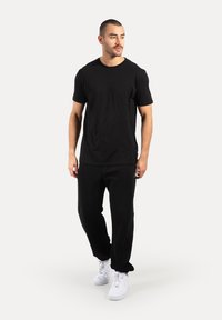 Conjunto de camiseta negra de manga corta y pantalones negros, con un corte relajado y textura suave, combinado con zapatillas deportivas blancas.