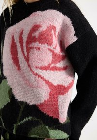 Černý pletený svetr s velkým designem růže v růžové a červené barvě s zelenými akcenty. Textilie má měkký, strukturovaný vzhled.