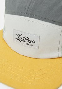 Baseballkappe mit gelb-schild und grauen, weißen und hellgrünen Paneelen. Verfügt über einen gestickten Logo-Patch mit der Aufschrift "Lil' Boo Copenhagen."