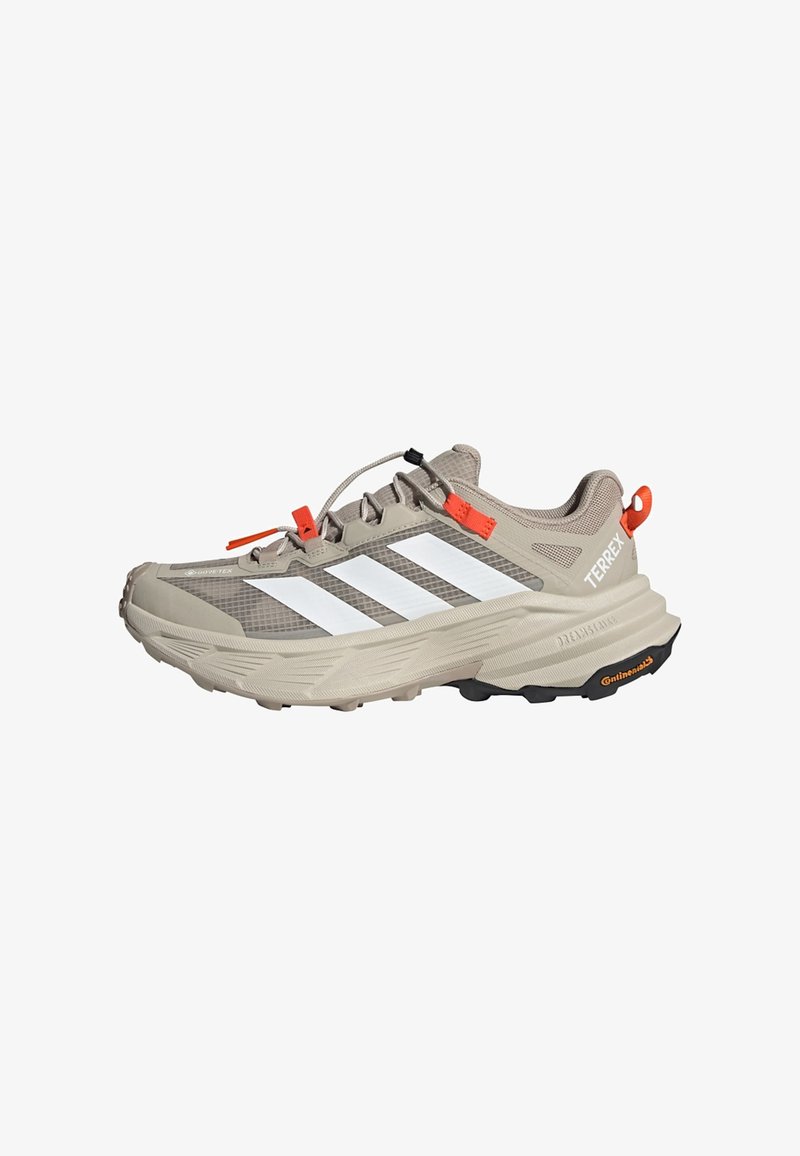 Chaussure de trail Adidas Terrex beige clair avec bandes blanches, languette orange et semelle texturée avec logo Continental.