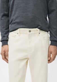 Vaqueros blancos de denim con diseño de pierna recta, presillas para cinturón y bolsillos delanteros, combinados con una camiseta gris de manga larga.