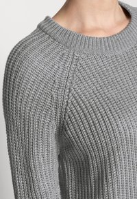 Maglione grigio lavorato a maglia con una texture a coste, scollatura rotonda e maniche raglan. Il tessuto appare morbido e spesso.