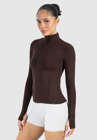 Bruine sportjack met ritssluiting, hoge kraag, lange mouwen en voorzak met rits. Gemaakt van rekbaar materiaal voor actieve kleding.
