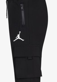 Jambe de pantalon noire avec une poche zippée, une poche cargo à rabat et un logo Jumpman blanc près de la poche supérieure.