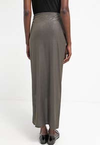 Maxikjol i metallisk brons tyg, med en slät textur och åtsittande midja, som sträcker sig ner till anklarna. Svarta ballerinas bärs.