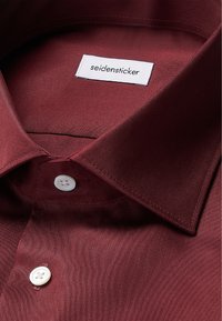 Bordeauxkleurig stoffen overhemden met een klassieke kraag, witte knoopsluitingen en een gladde satijnen textuur. Etiket leest "seidensticker."