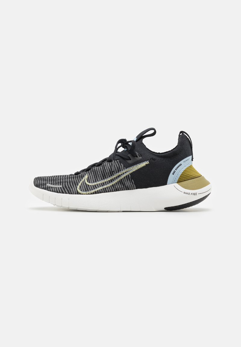 Nike Free sportcipők fekete kötött felsőrésszel, textúrált mintával, sárga díszítéssel és fehér talppal. Felszerelt fűzőkkel és logóval a sarkon.