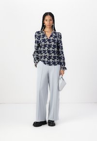 Blusa stampata floreale in navy e crema con maniche a sbuffo, abbinata a pantaloni ampi grigi chiari e scarpe chunky nere. Borsa a mano argentata.