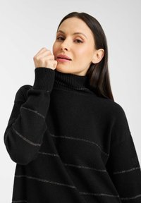 Zwarte coltrui met ribbelhals, voorzien van metallic horizontale strepen. Zachte textuur en een losse pasvorm met verlaagde schouders.