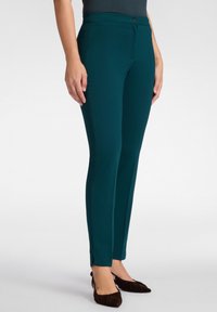 Türkise, figurbetonte Hose aus dehnbarem Material mit einem Frontknopfverschluss, seitlichen Schlitzen an den Knöcheln und einer glatten Textur.