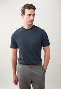 Navy blue crew neck t-shirt made of soft fabric, paired with light gray trousers. The t-shirt has short sleeves and a smooth texture.