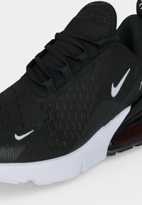 Μαύρο αθλητικό παπούτσι Nike με λευκή σόλα, εμφανές αερόθαλαμο στη φτέρνα, μαύρα κορδόνια και λευκά λογότυπα Nike swoosh στο πλάι και στην περιοχή των δακτύλων.