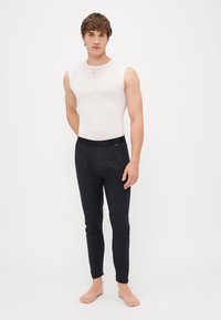 Hvid ærmeløs skjorte parret med sorte tætsiddende bukser. Begge beklædningsgenstande er lavet af strækbart stof med en glat tekstur og et minimalistisk design.