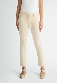 Pantaloni bej cu o curea împletită, având o croială slim fit și o textură netedă, acompaniați de balerini aurii cu vârf ascuțit și detaliu cu fundiță.