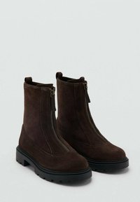 Botas de tobillo de ante marrón con caña alta, que cuentan con un cierre delantero, una superficie texturizada y una suela de goma negra resistente.