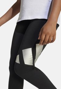 Leggings negras con un patrón geométrico plateado metálico en el costado, confeccionados con un tejido elástico que proporciona comodidad y flexibilidad.