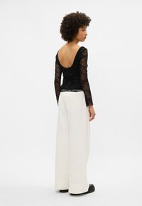 Μαύρη δαντελένια μπλούζα με μακριά μανίκια και βαθύ ανοιχτό πίσω μέρος, συνδυασμένη με λευκά παντελόνια ψηλής μέσης και μαύρα πλατφόρμες.