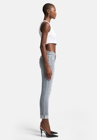 Grijze high-waisted jeans met een taps toelopende pijp, opgerold bij de enkel, gecombineerd met een witte crop top en zwarte puntige hakken.