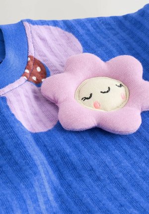 Blå tekstureret stof med et pink blomsterapplikation, der har et smilende ansigt med lukkede øjne og rosige kinder.