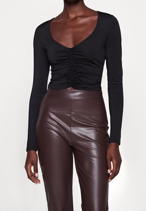 Schwarzes Langarmshirt mit tiefem V-Ausschnitt und gerafften Details an der Vorderseite, kombiniert mit braunen High-Waist-Hosen aus Kunstleder.